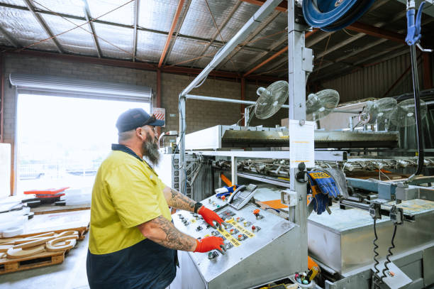 worker wearing gloves and safety gear operates a control panel in a spacious industrial2202658175